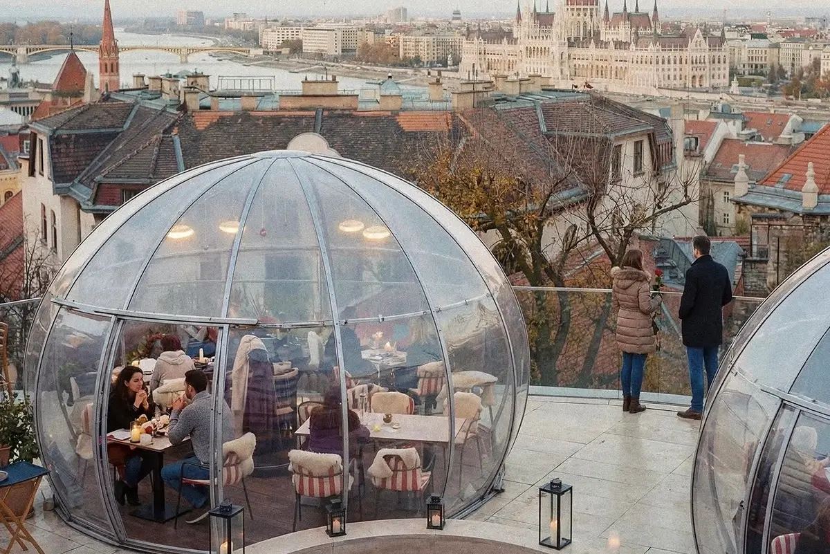 Polikarbonát igloo vacsorázó vendégekkel egy budapesti tetőteraszon, háttérben a Parlament