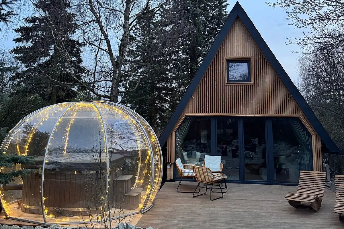 Fényfüzéres igloo dézsafürdővel egy faház teraszán