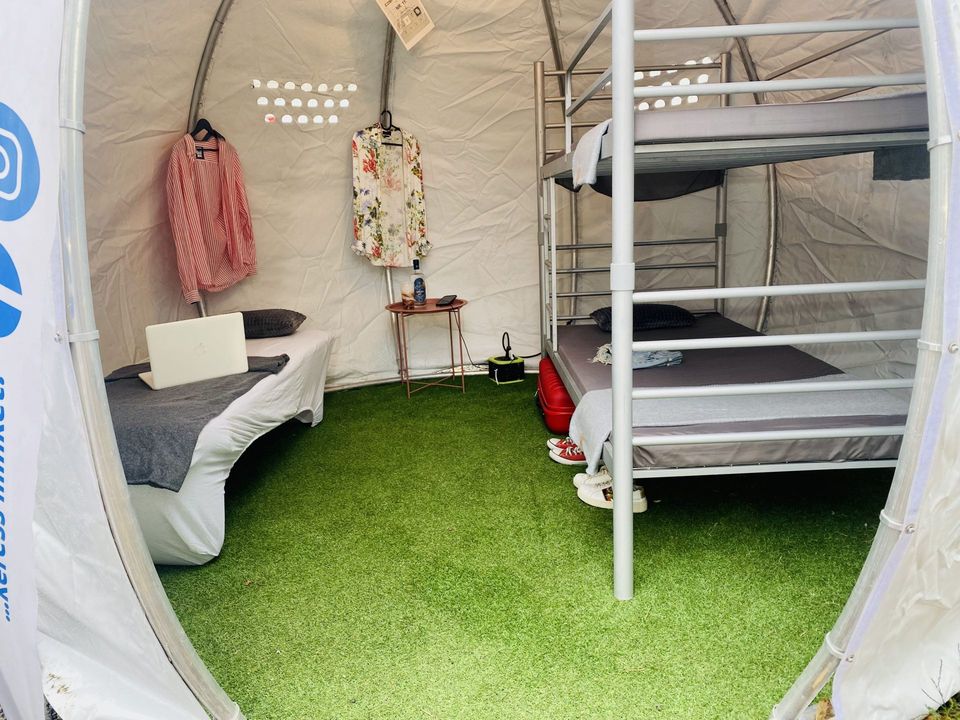 Glamping igloo belseje nappal: ágy, emeletes ágy, kis asztal, akasztók és műfüves aljzat