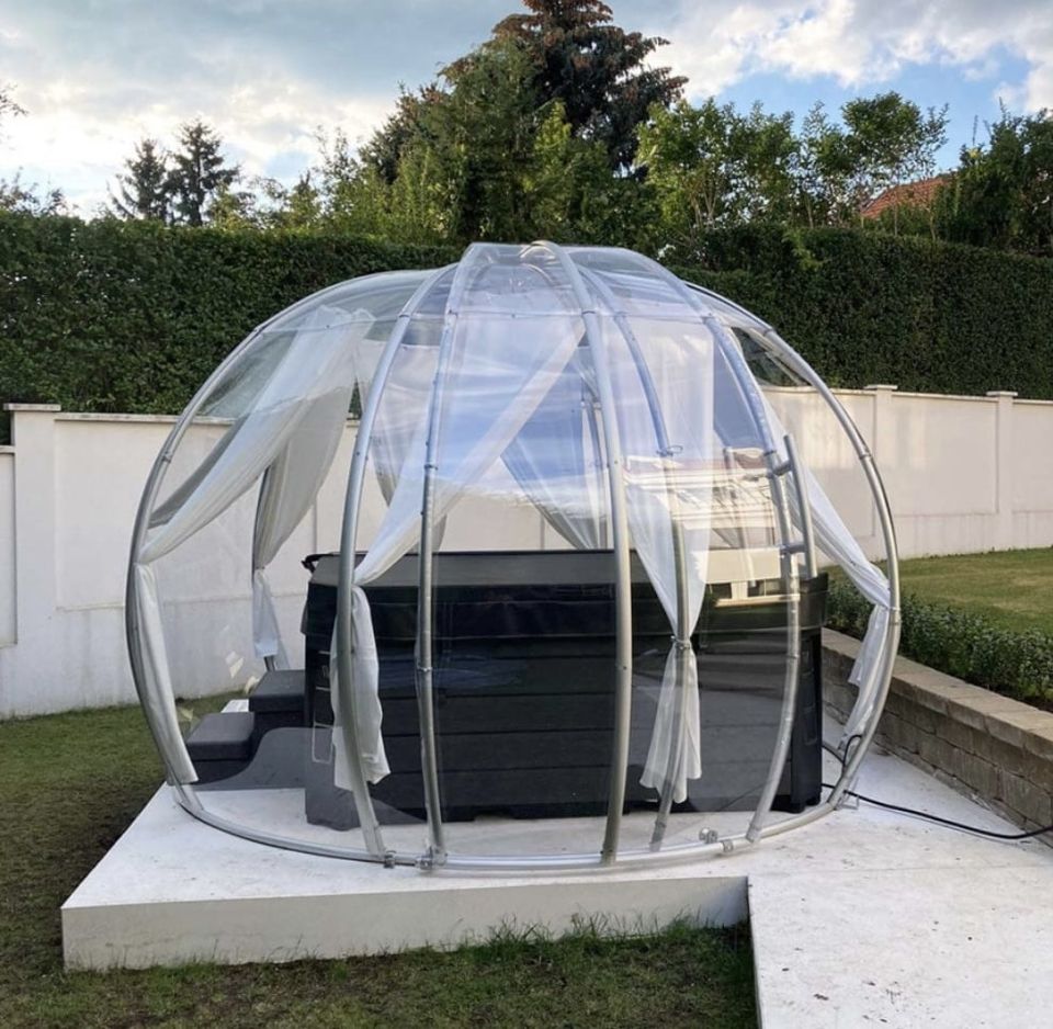 Polycarbonat-Igloo über einem Whirlpool auf weißem Betonsockel in einem Garten mit Hecke