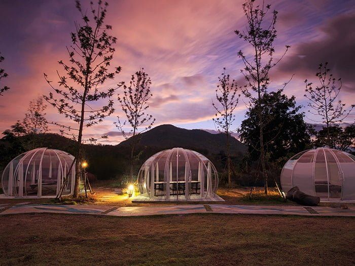 Három glamping igloo alkonyatkor, háttérben hegyek