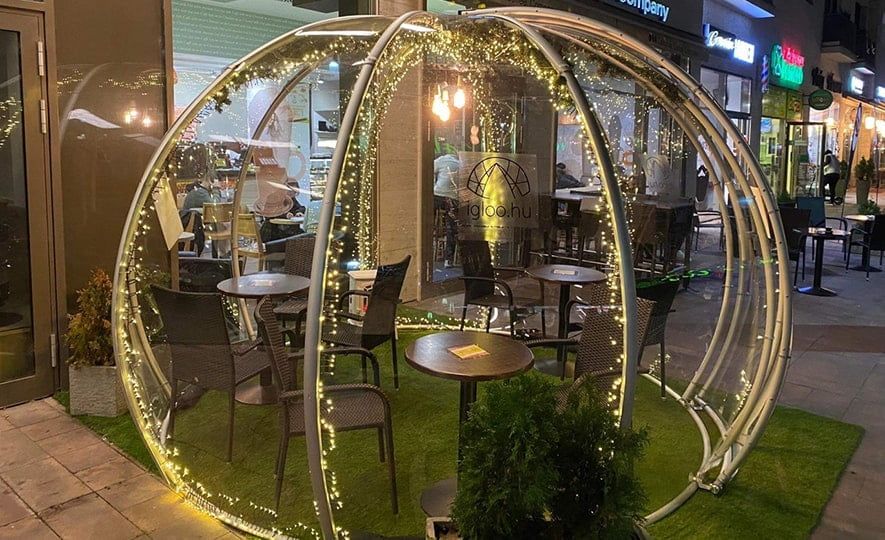 Fényfüzéres polikarbonát igloo műfűvel és asztalokkal egy kávézó előtt este
