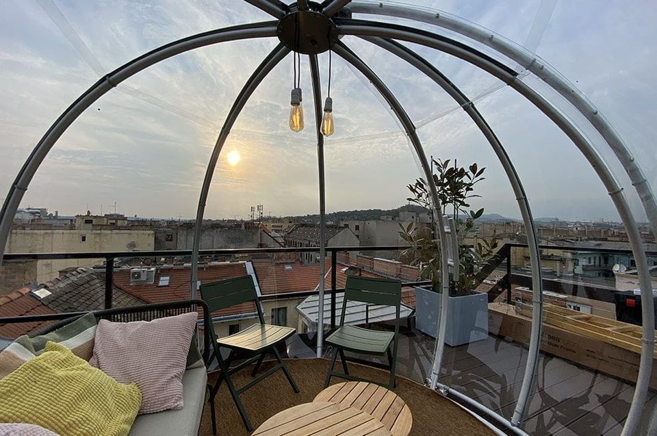 Igloo belseje lounge bútorokkal és Edison-izzókkal egy tetőteraszon naplementekor